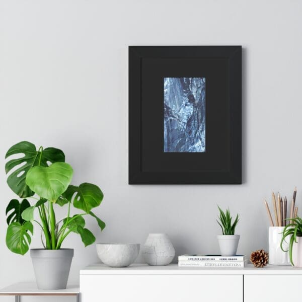 Framed abstract art above plants on shelf.